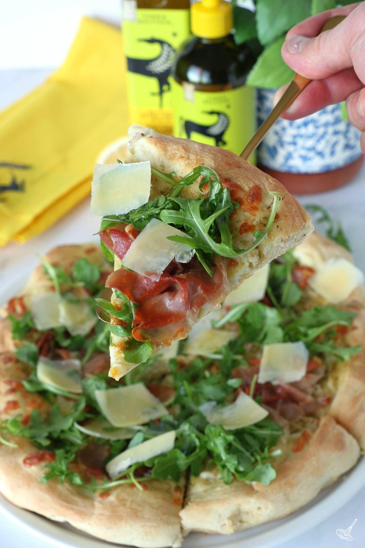 Someone holding up a slice of Prosciutto Arugula Pizza.