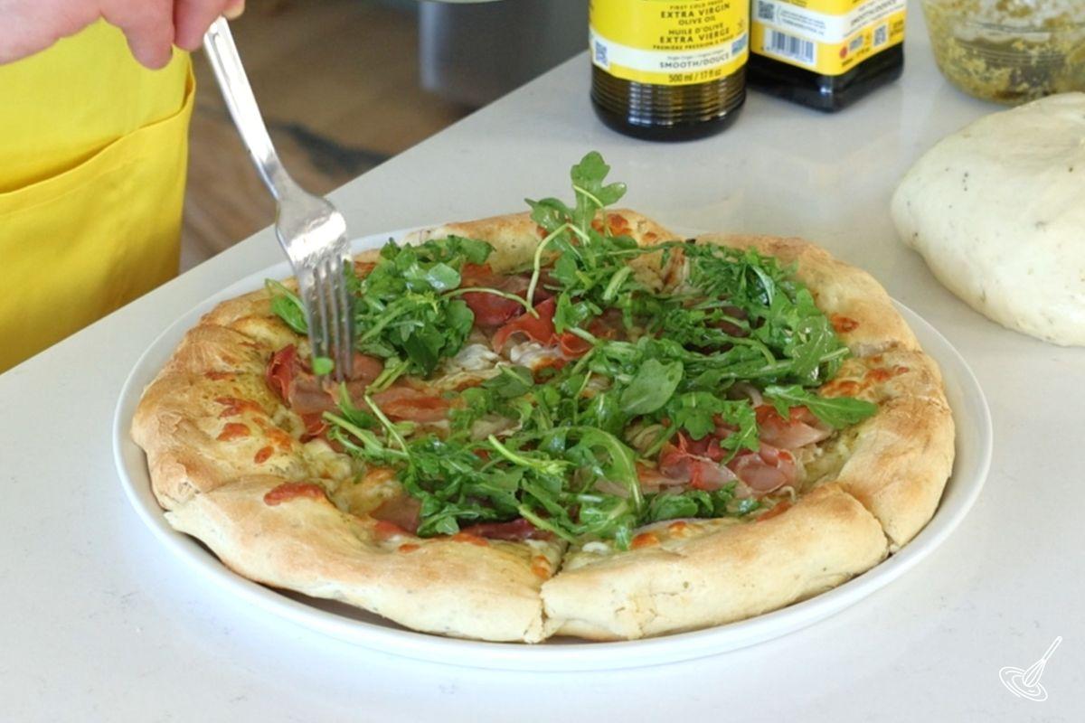 Someone placing arugula on top of prosciutto pizza. 