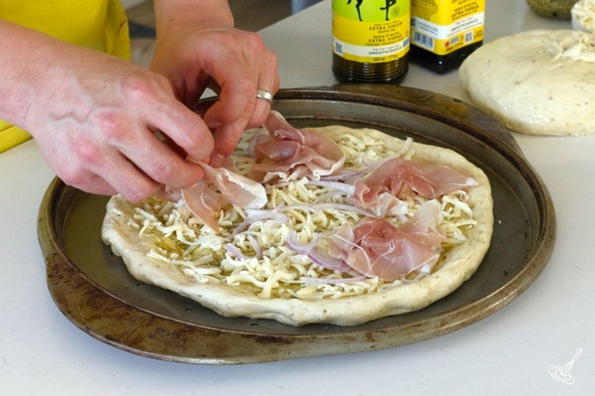 Someone placing prosciutto on top of the pizza.
