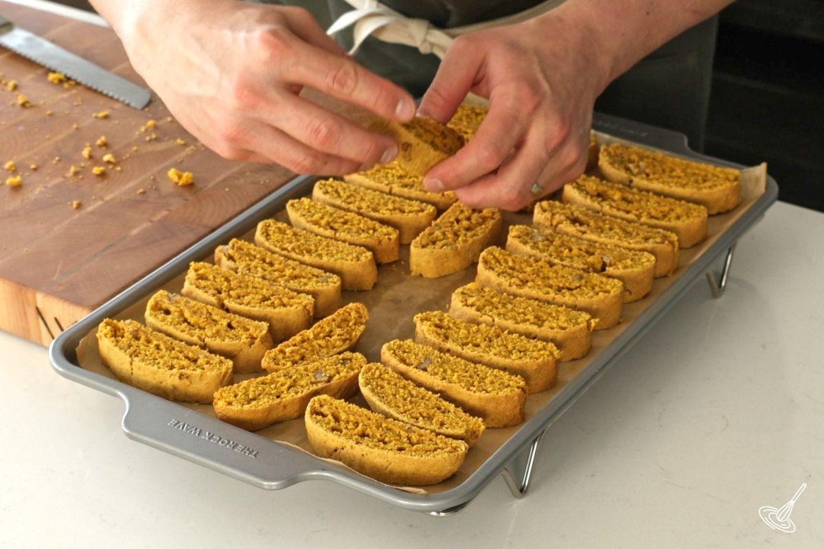 Someone placing the sliced biscotti on a baking tray.