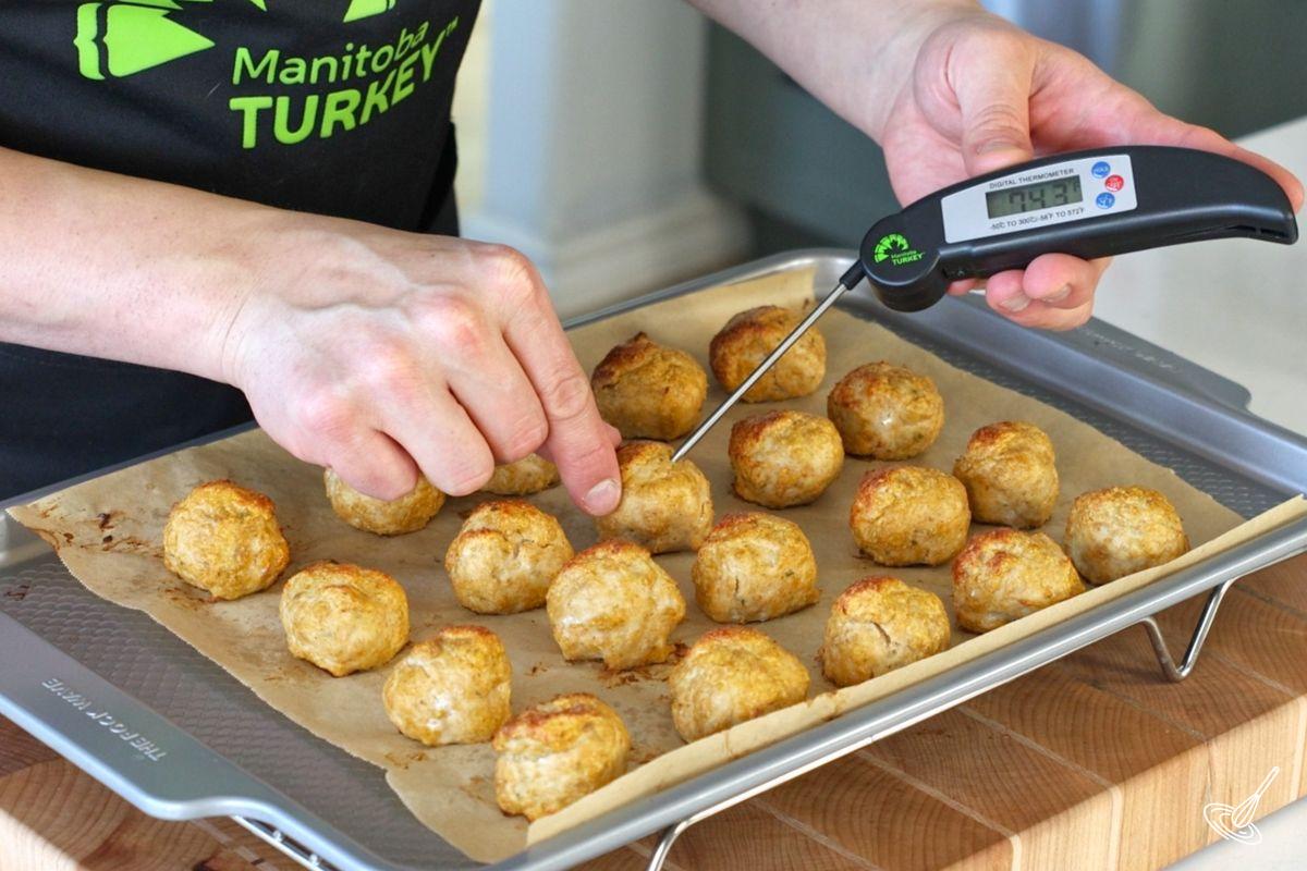 Someone using a probe thermometer to check the doneness  of the baked pumpkin meatballs.  