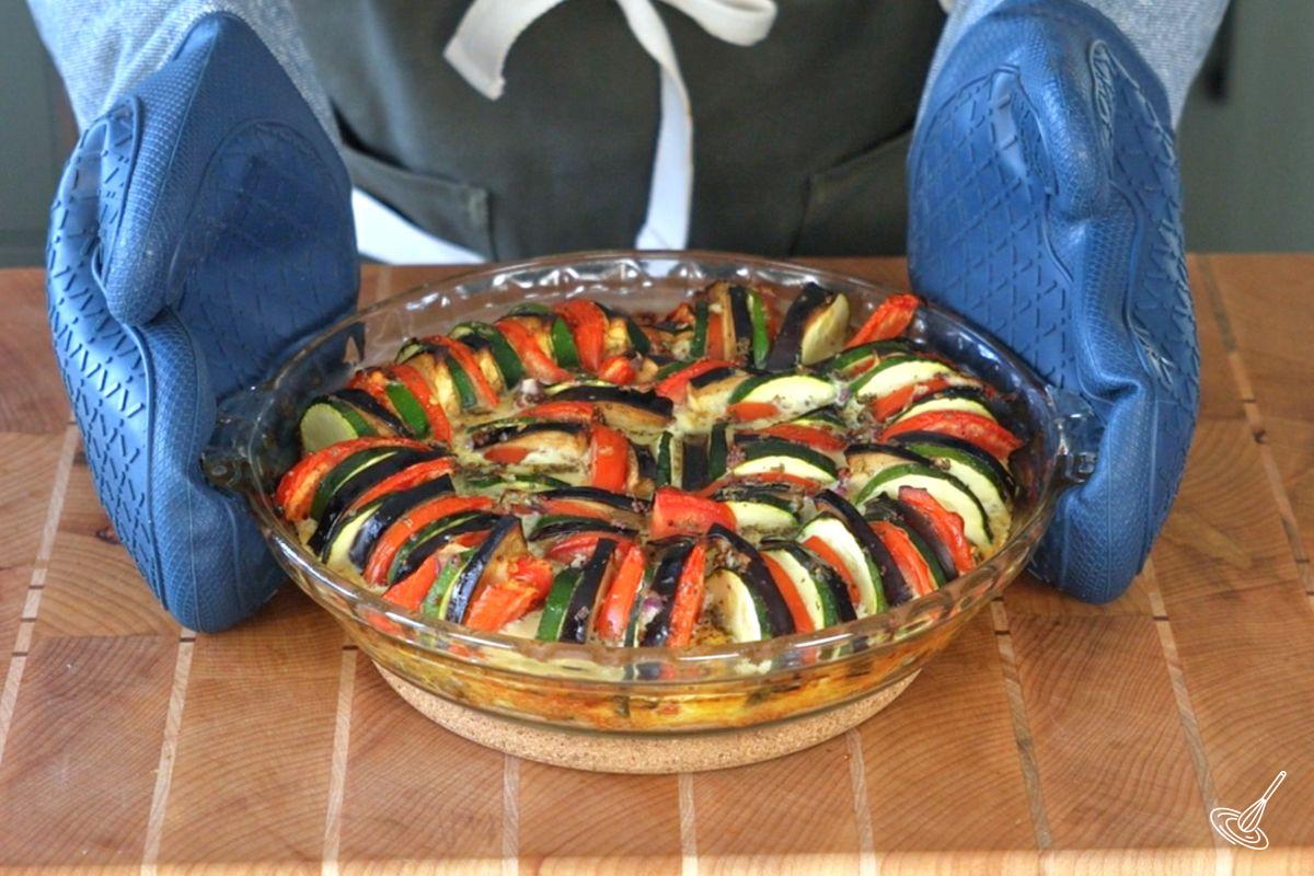 Someone taking a baked ratatouille egg out of the oven. 