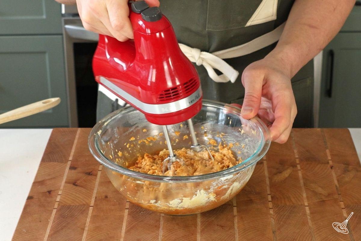 Someone using a hand blender to add pumpkin puree to a bowl.