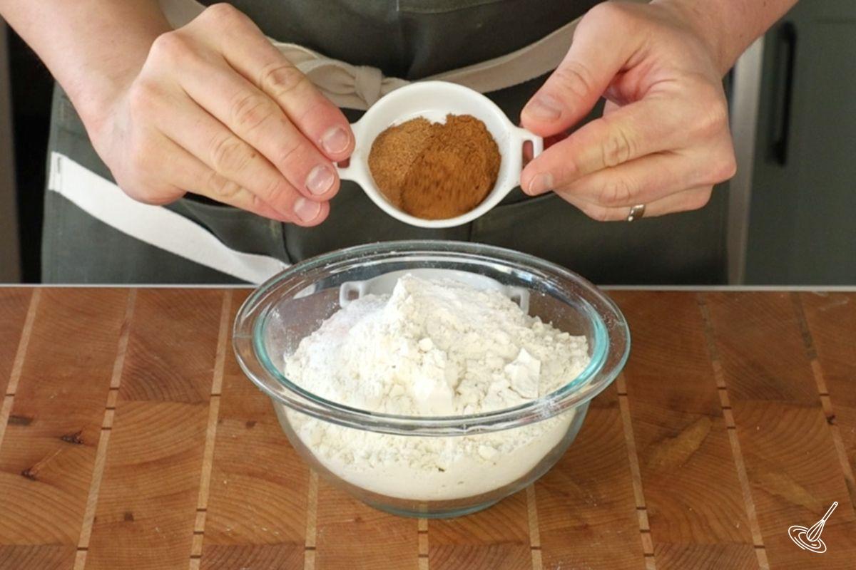 Someone adding cinnamon to a bowl of flour.