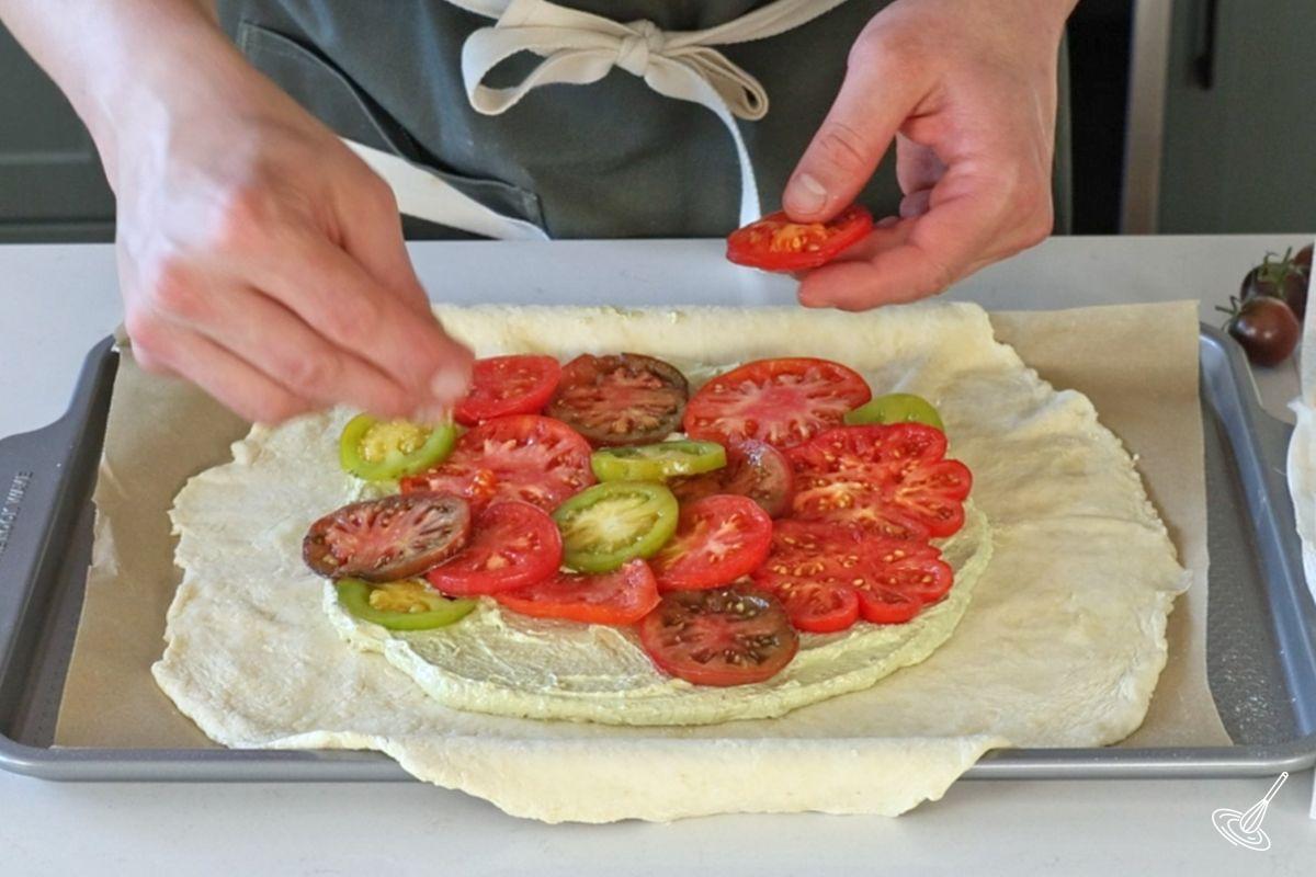 Quelqu’un disposant des tranches de tomates sur une galette.