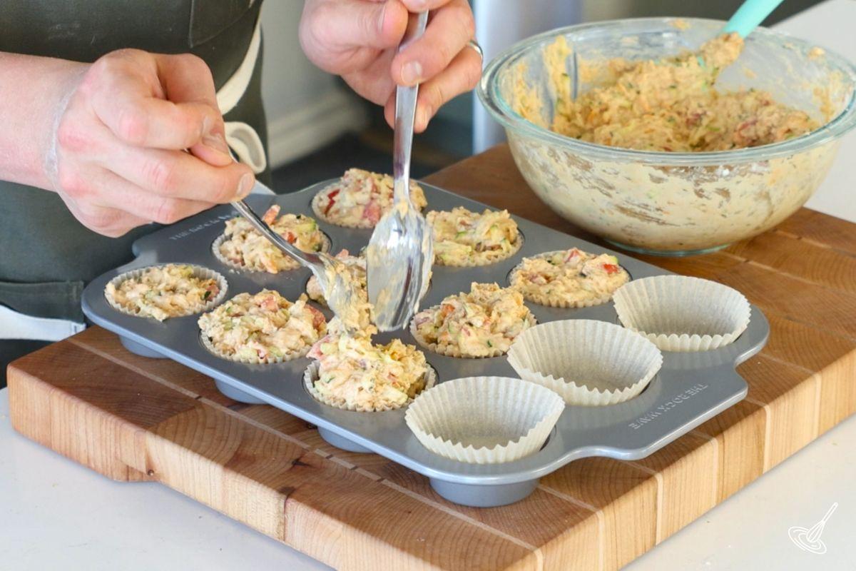 Quelqu’un utilise des cuillères pour répartir la pâte à muffins dans un moule à muffins. 