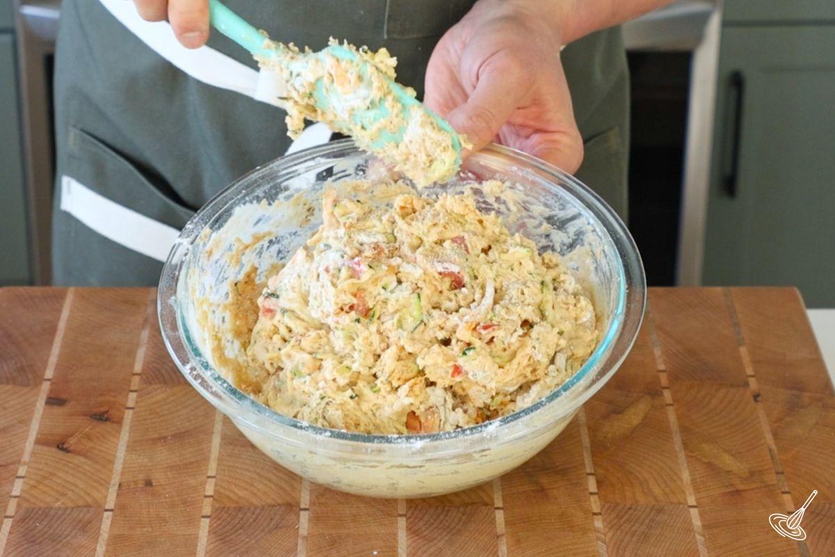 Quelqu’un utilise une spatule en caoutchouc pour incorporer le fromage dans la pâte à muffins tomate-courgette.