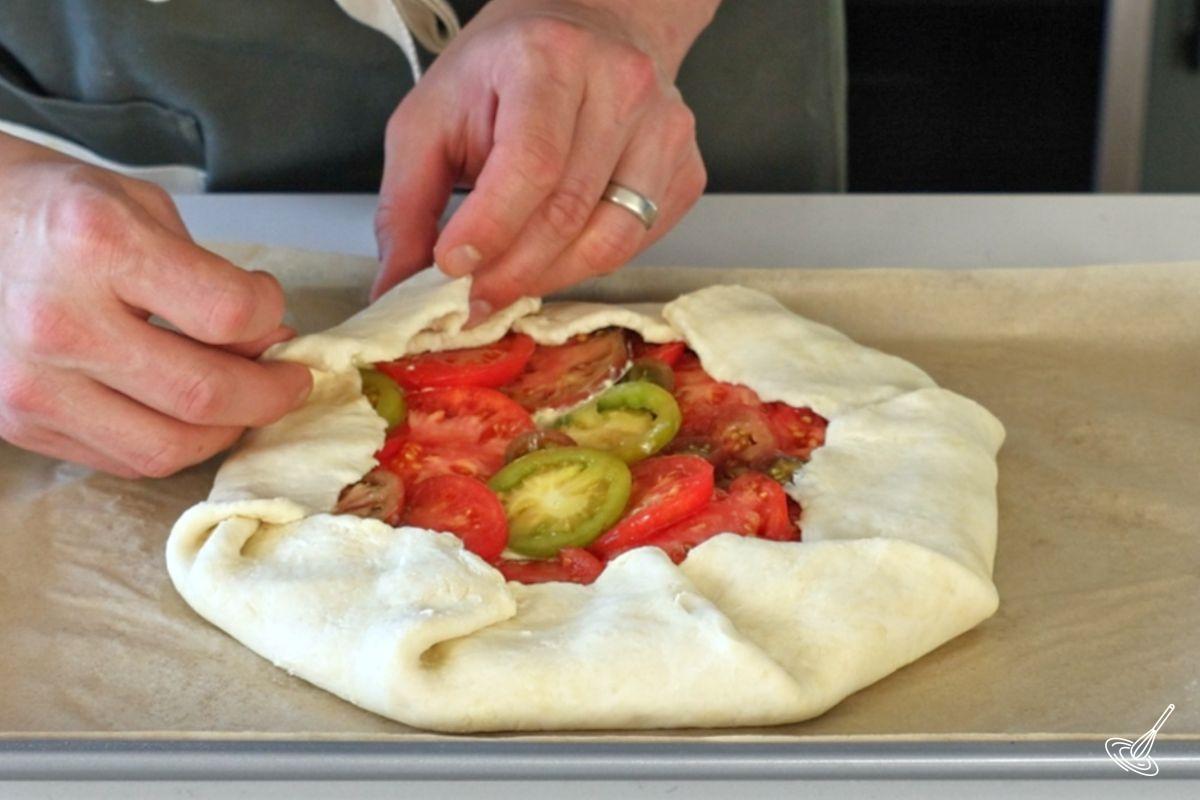Quelqu’un repliant les bords de la galette à la tomate et au pesto.