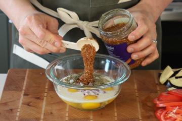 Someone adding mustard to a bowl of egg mixture.