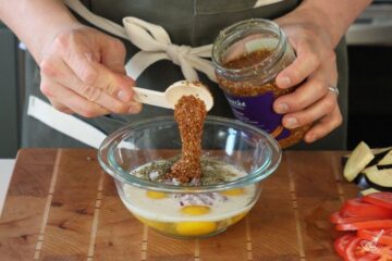 Someone adding mustard to a bowl of egg mixture.