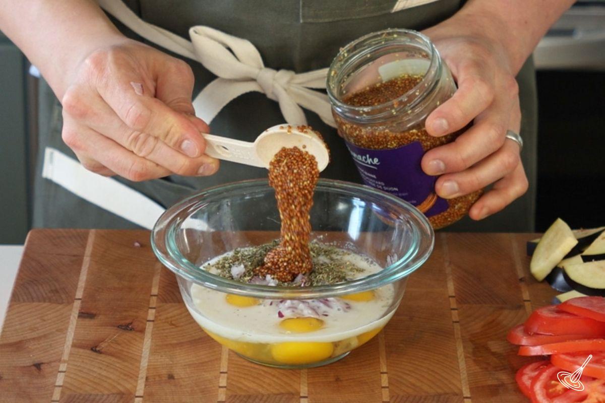 Someone adding whole grain mustard to a bowl of eggs.