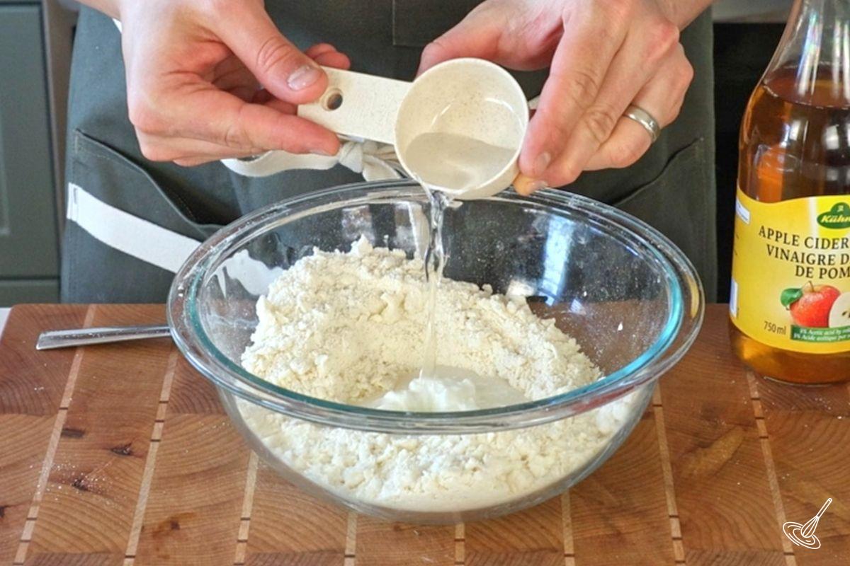 Quelqu’un ajoutant de l’eau dans un bol de pâte à tarte.