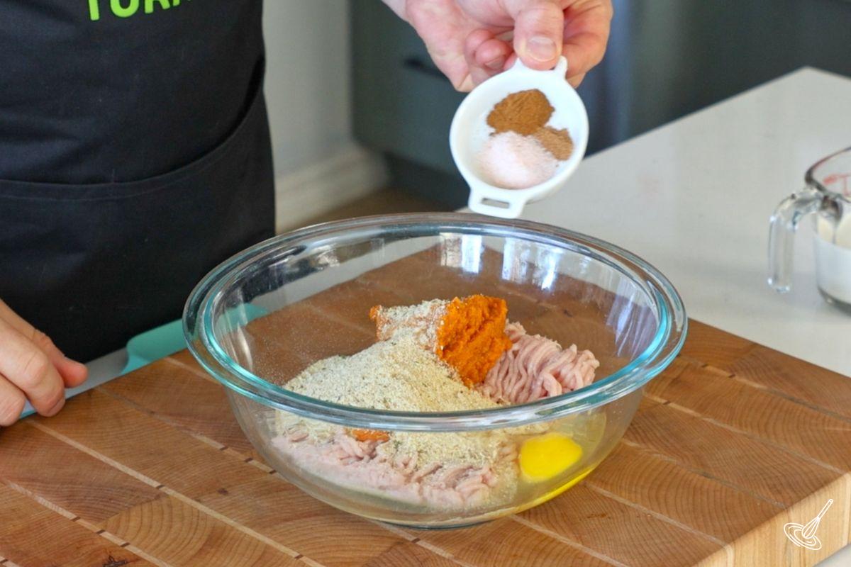 Someone adding spices to a bowl of ground turkey.