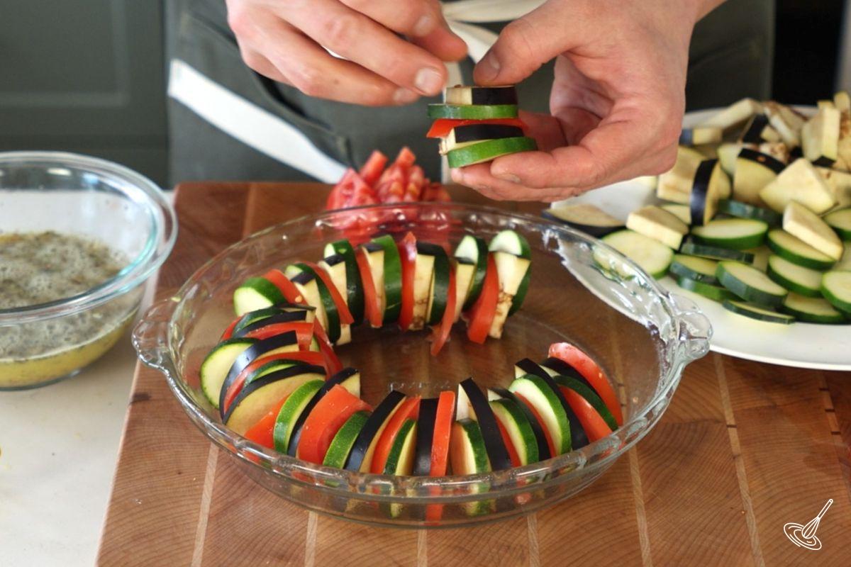Someone placing sliced vegetables vertically in a baking dish.