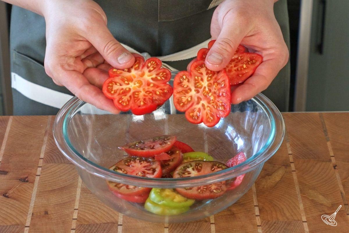 Quelqu’un ajoutant des tranches de tomates dans un grand bol.