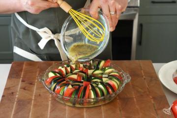 Someone pouring an egg mixture over a baking dish of vegetable slices.