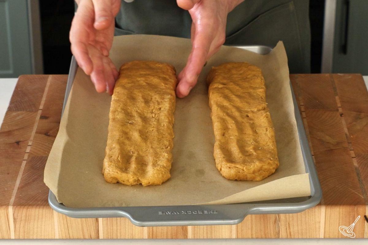 Someone shaping biscotti logs on a baking tray.