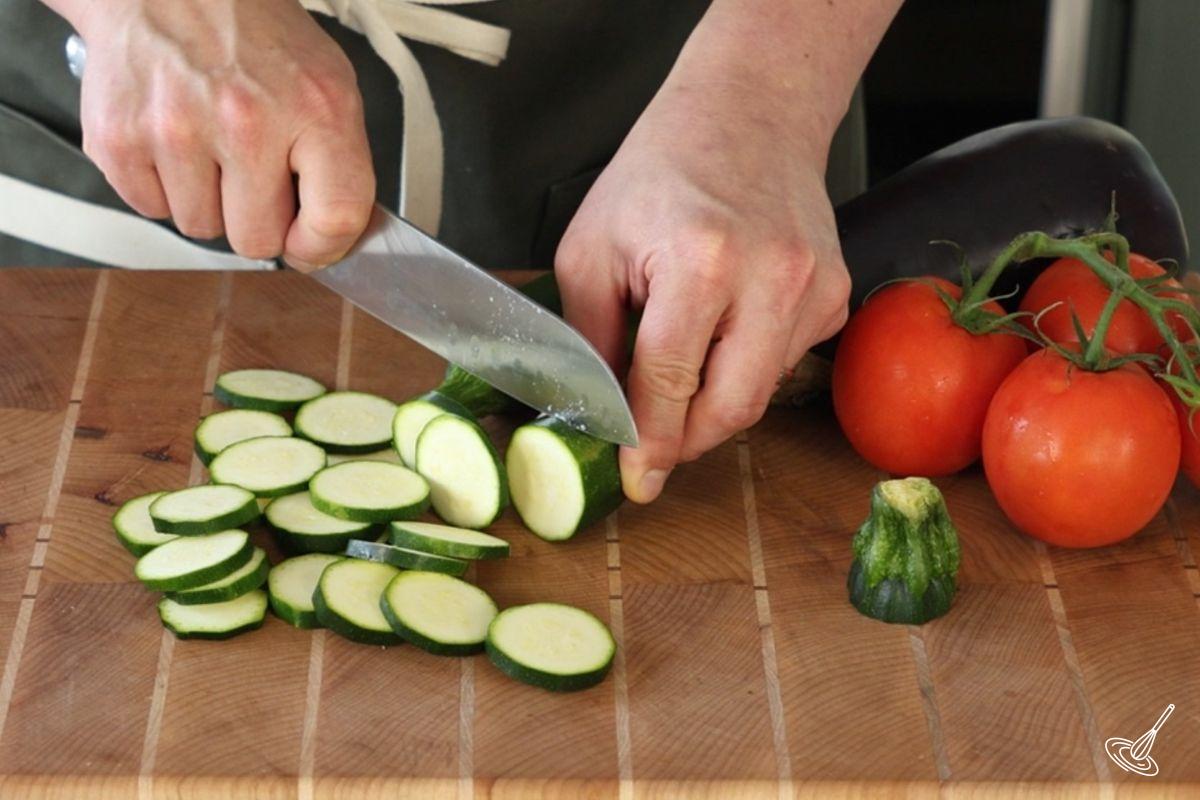 Someone cutting a zucchini into slices.