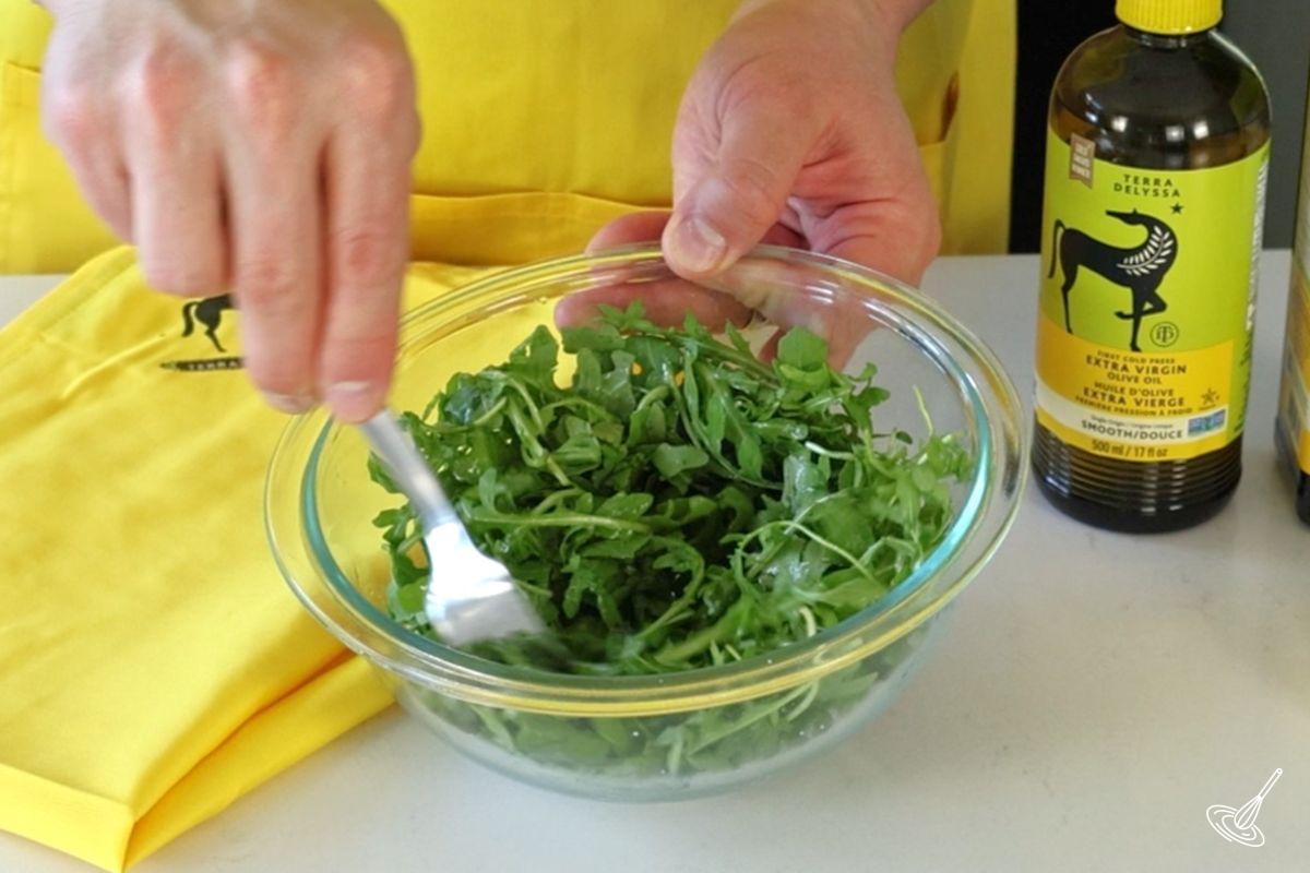 Someone using a fork to stir a bowl of arugula. 