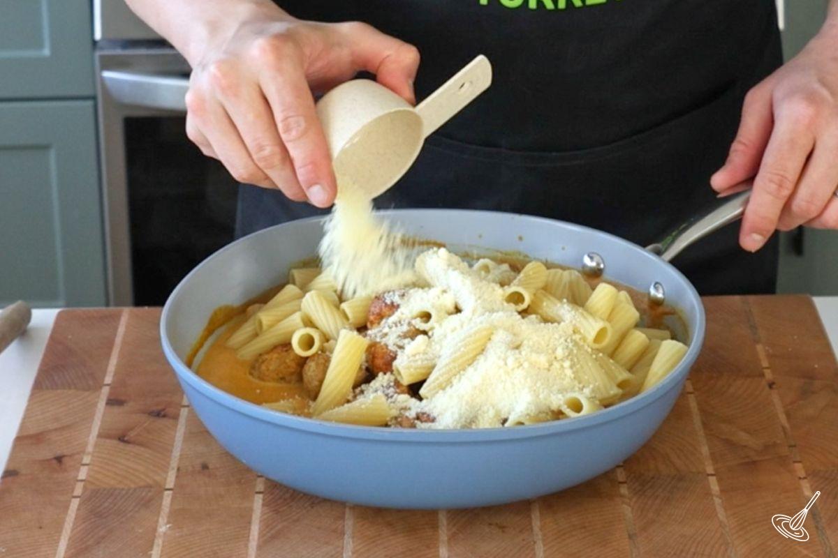 Someone adding parmesan cheese to a large pan of Pumpkin Turkey Meatballs. 