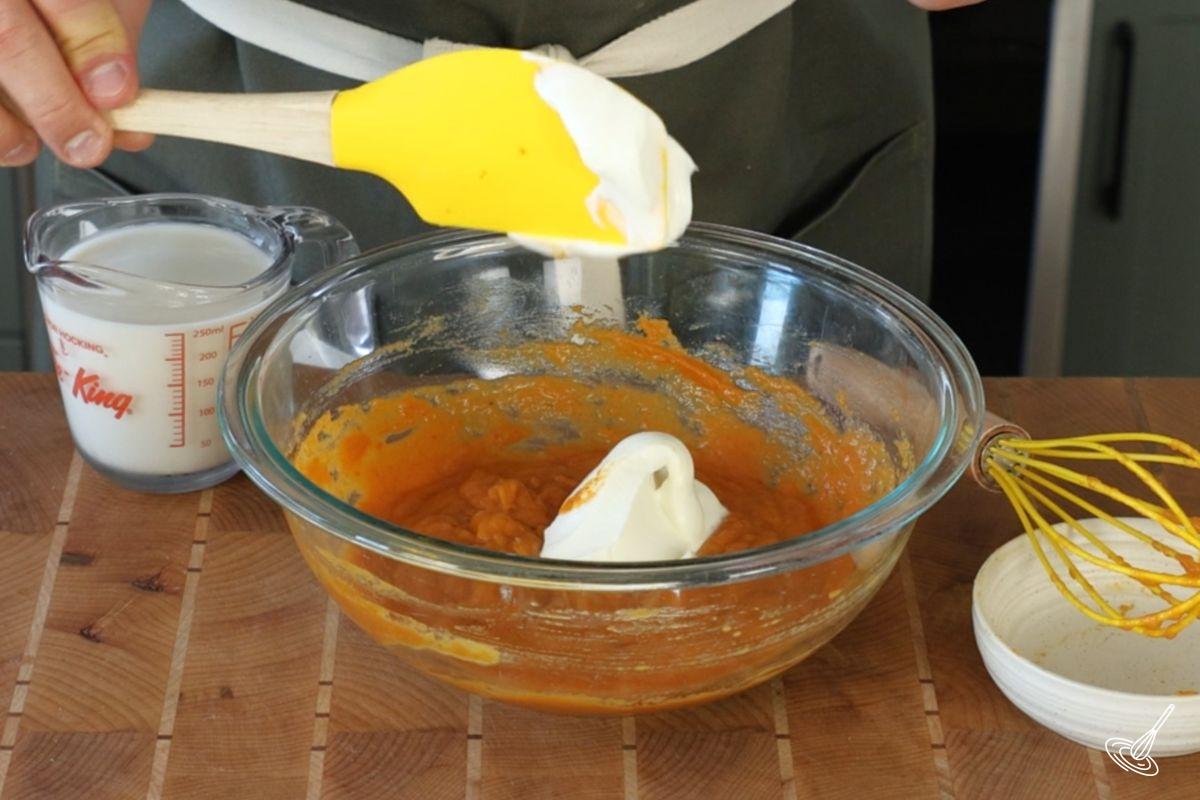 Someone adding greek yogurt to a bowl of pumpkin mixture.