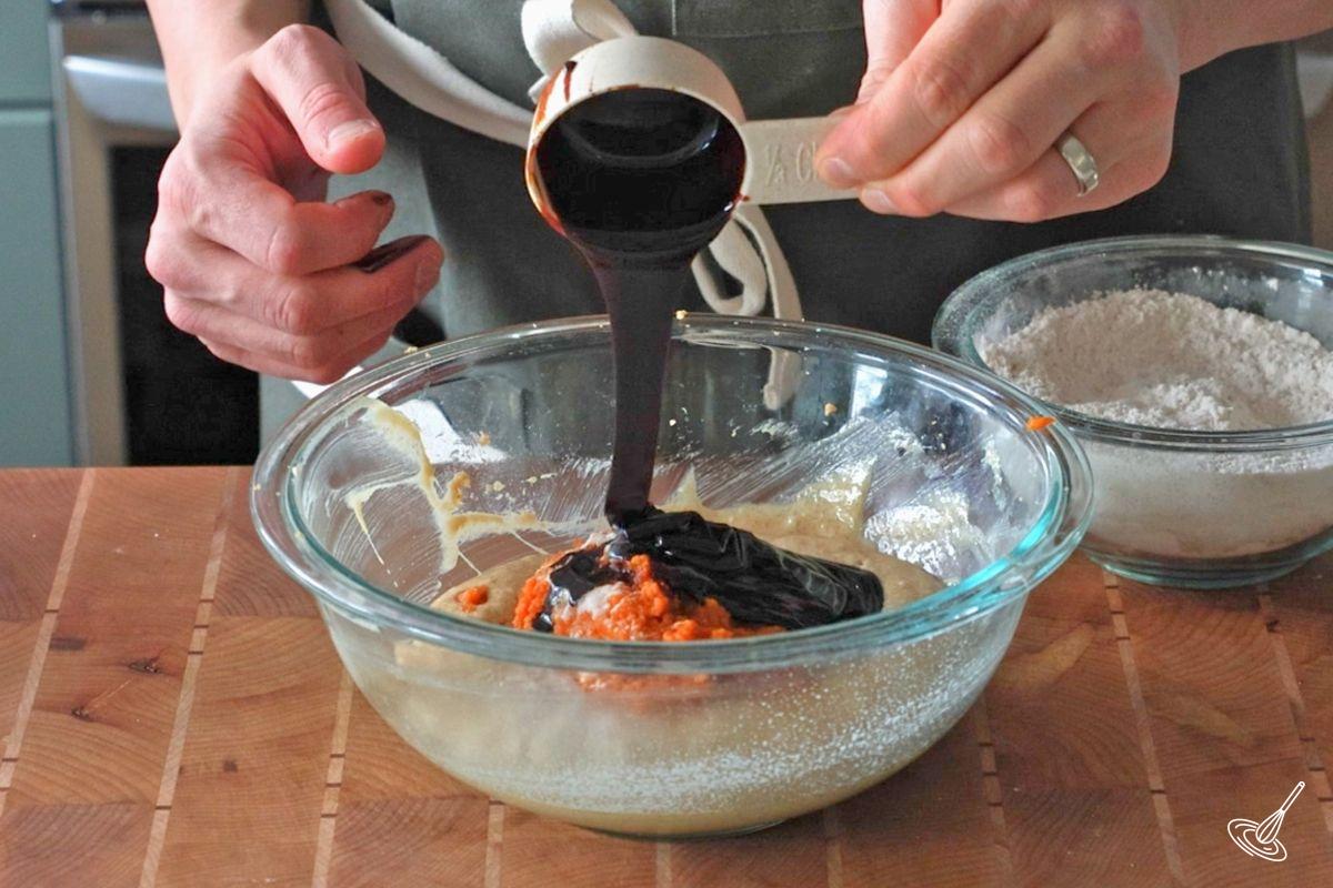 Someone adding molasses to a bowl of wet ingredients. 