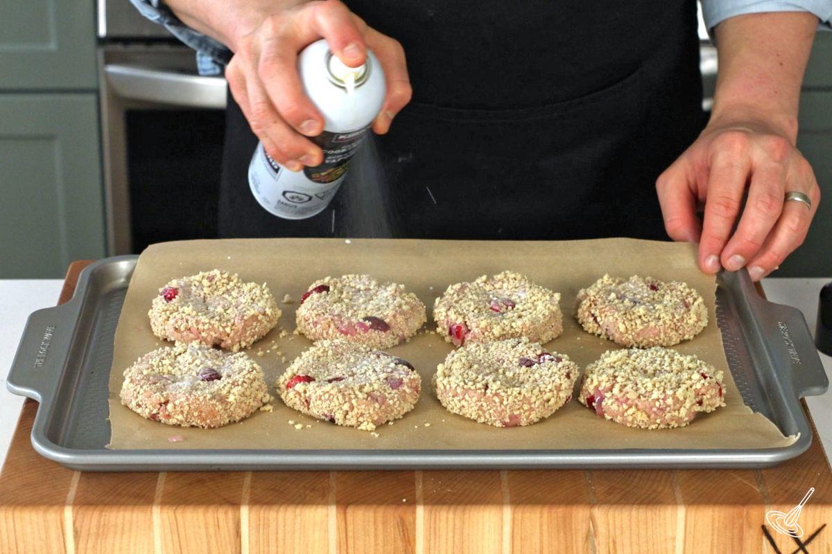 Someone spraying cooking oil over shaped turkey cranberry croquettes.