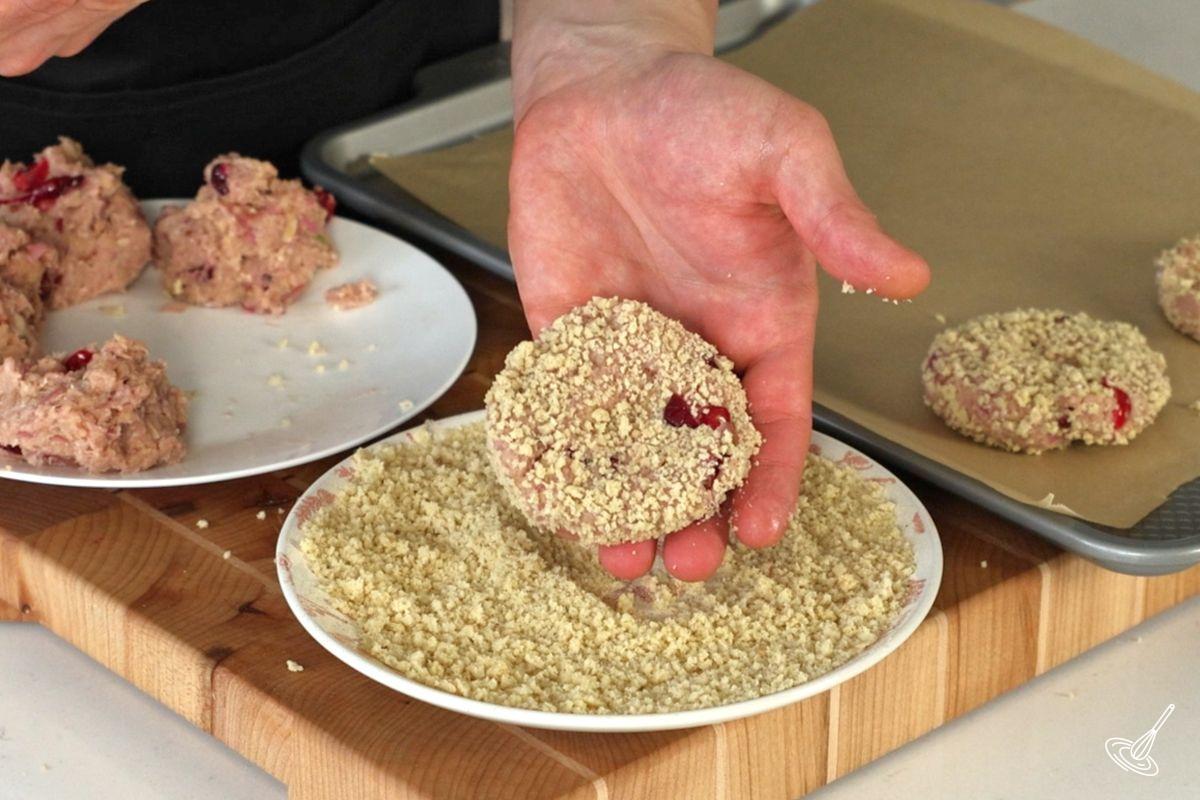 Someone placing a turkey cranberry croquette in a plate of panko crumbs.
