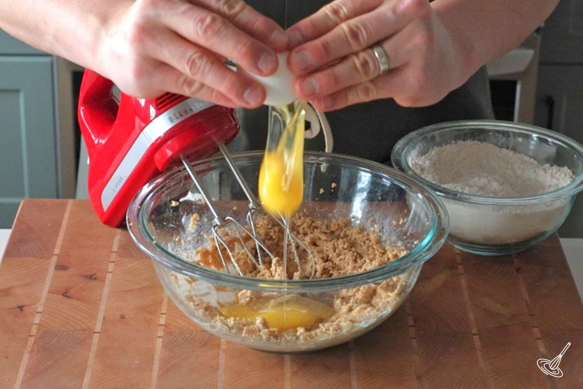 Someone cracking an egg into a bowl of creamed sugar.