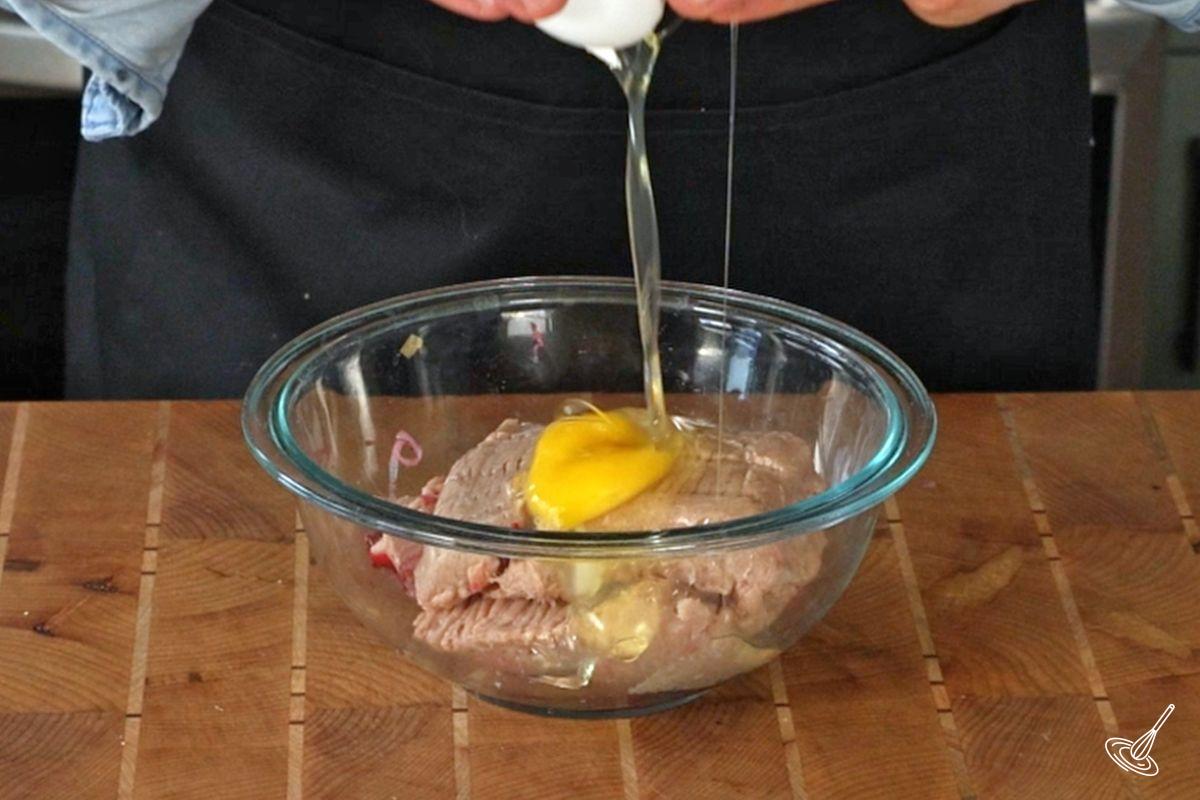 Someone adding an egg to a mixing bowl of ground turkey.