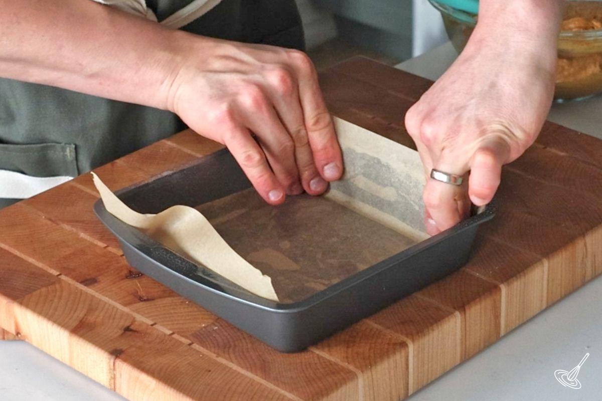 Someone lining a baking pan with parchment paper.
