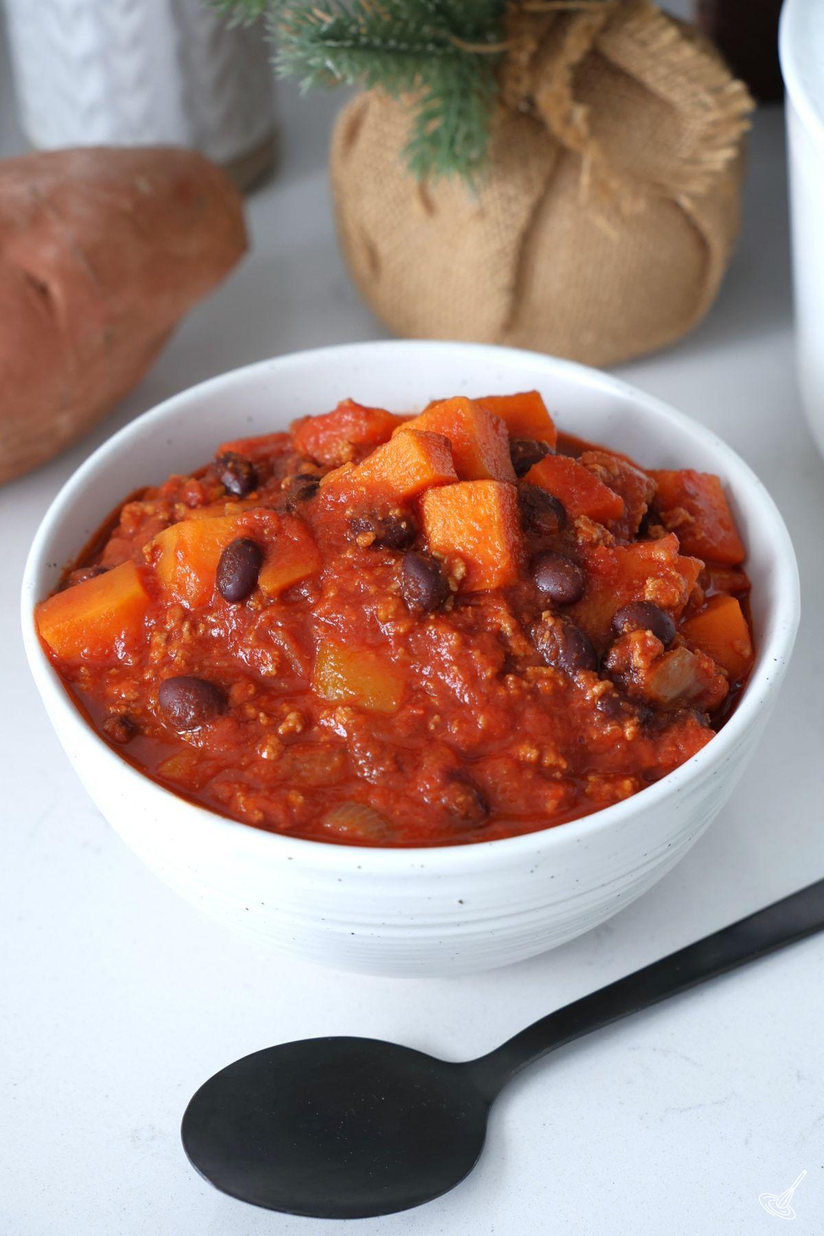 Un bol blanc de chili à la dinde et à la patate douce avec une cuillère noire. 