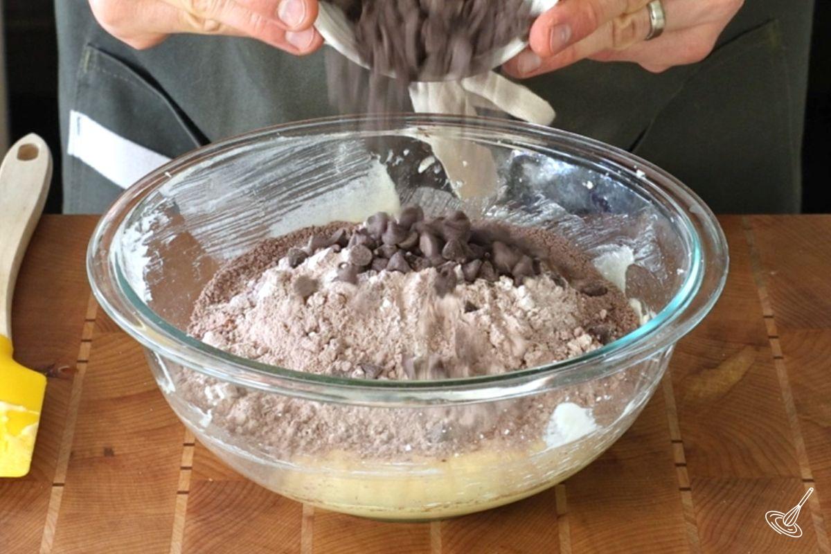 Someone combining flour and chocolate chips to a bowl of wet ingredients. 