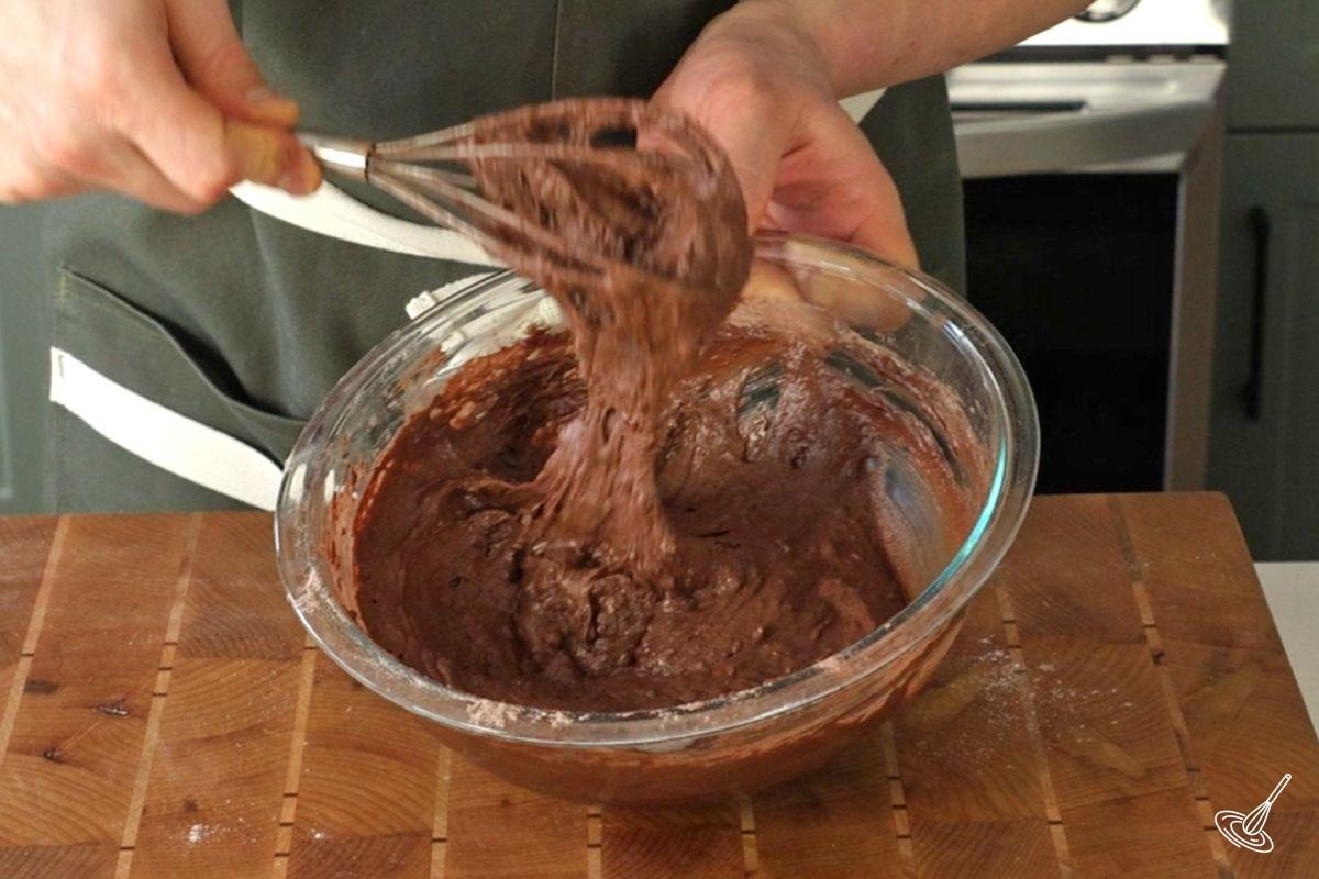 Someone using a whisk to mix chocolate orange loaf batter.