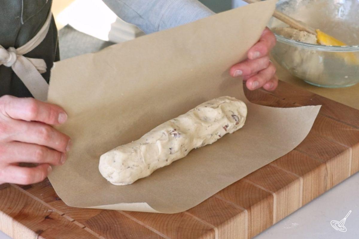 Someone rolling a log of shortbread dough in parchment paper.