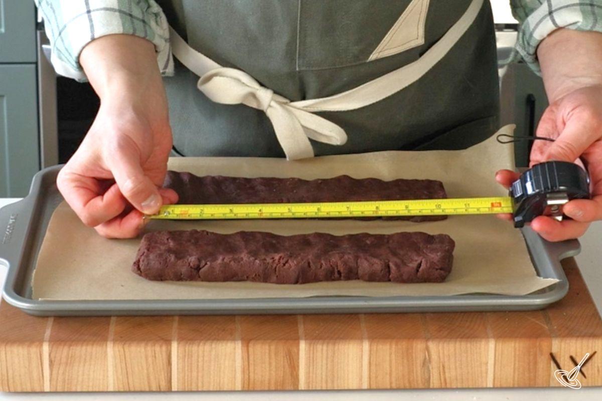 Someone using a measuring tape to make sure logs of biscotti dough are the right size.