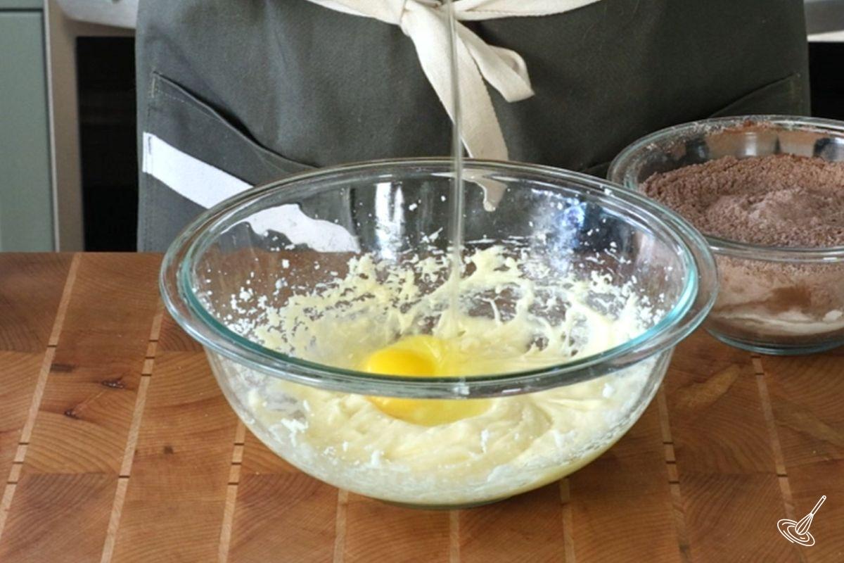 Someone adding an egg to a bowl of creamed butter and sugar.
