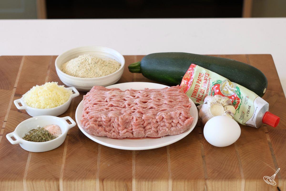 Ingrédients disposés sur une planche à découper pour préparer des boulettes, notamment de la dinde hachée, de la courgette, un œuf et de la chapelure.