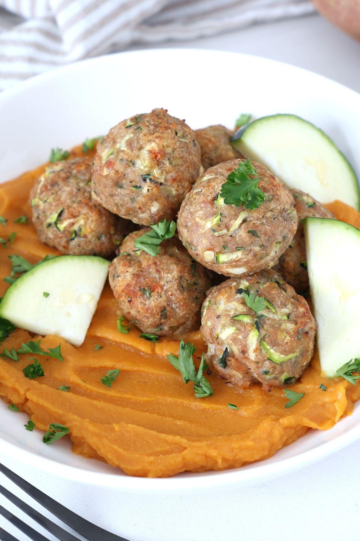 Boulettes de dinde et courgette cuites au four, servies sur un bol de purée de patates douces.