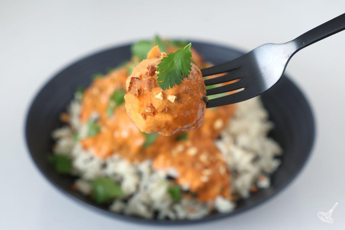 Someone holding a fork with a turkey meatball with coconut curry sauce .