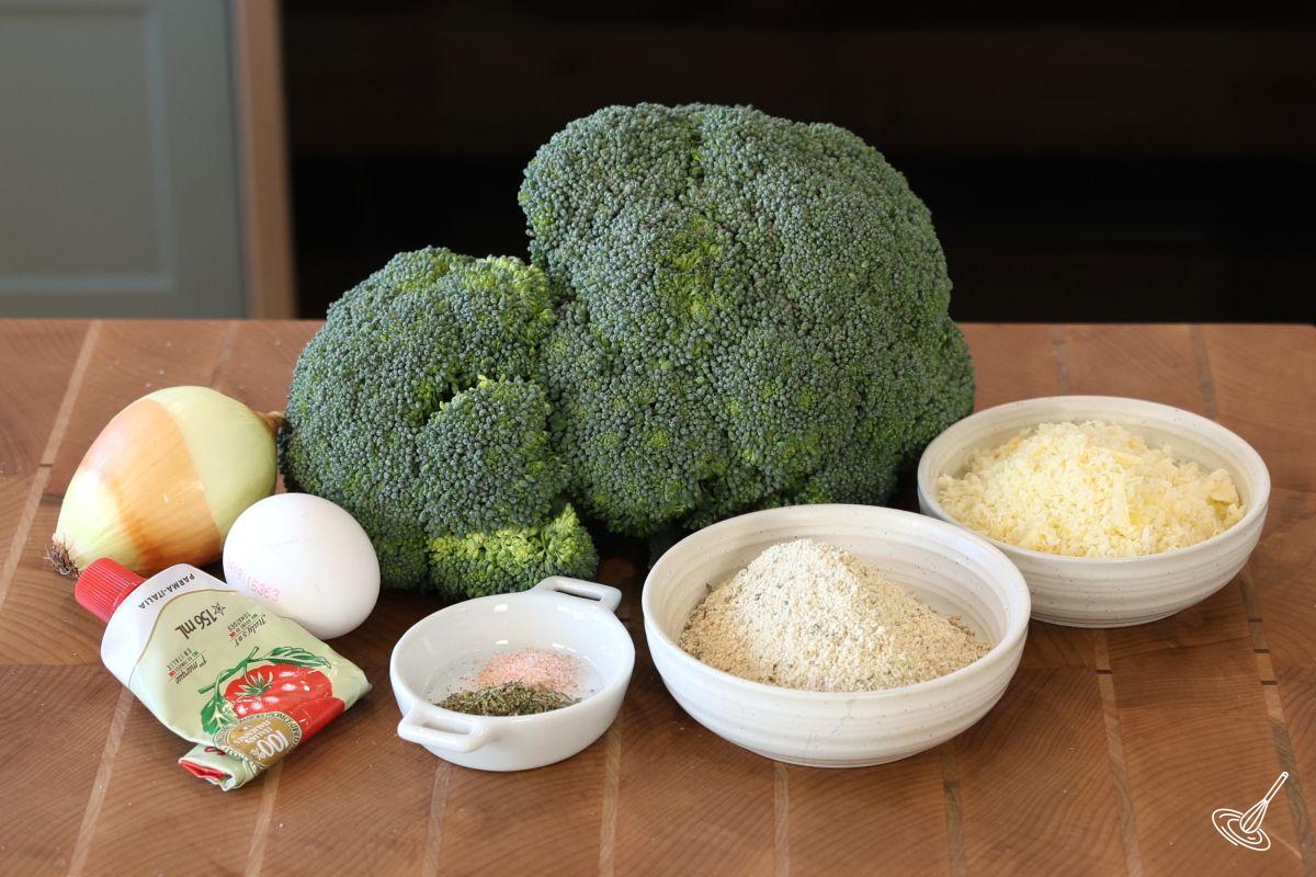 Ingredients on a cutting board including broccoli, onion, egg, tomato paste, bread crumbs and grated parmesan.