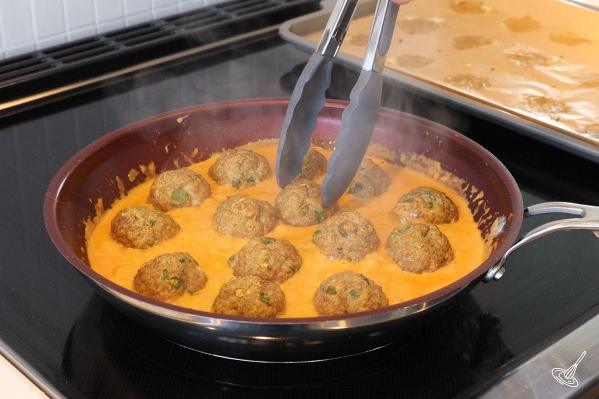 Someone placing cooked turkey meatballs into a pan of coconut curry sauce.