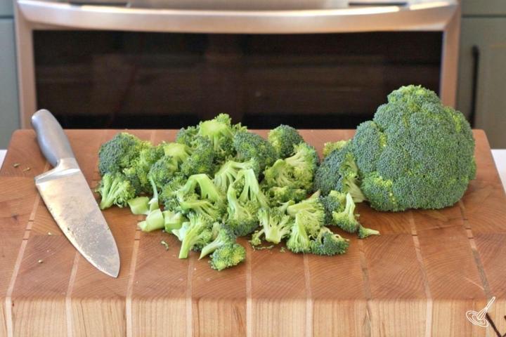 Broccoli cut into florets on a wooden cutting board. 