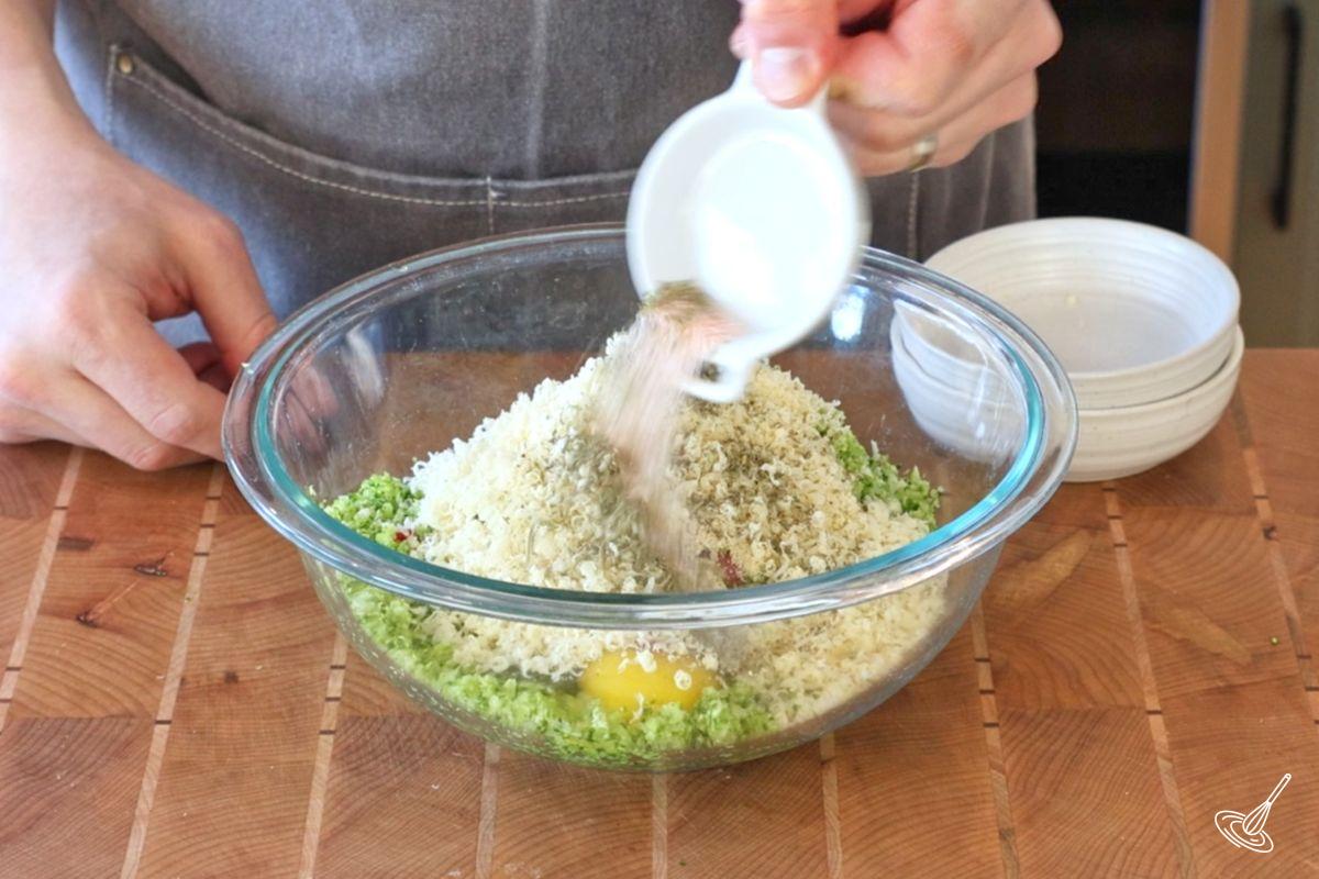 Someone adding seasoning to a large bowl of broccoli rice and parmesan. 