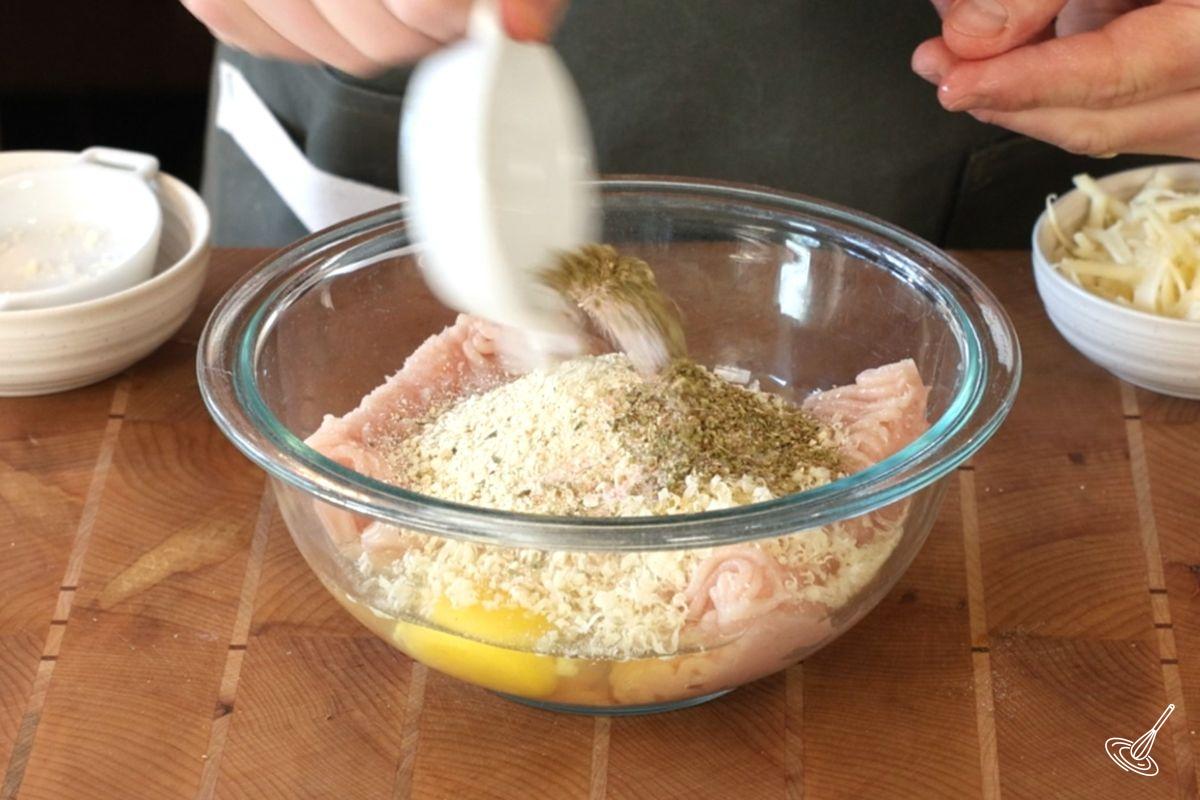 Someone adding the ingredients to make meatballs to a bowl.