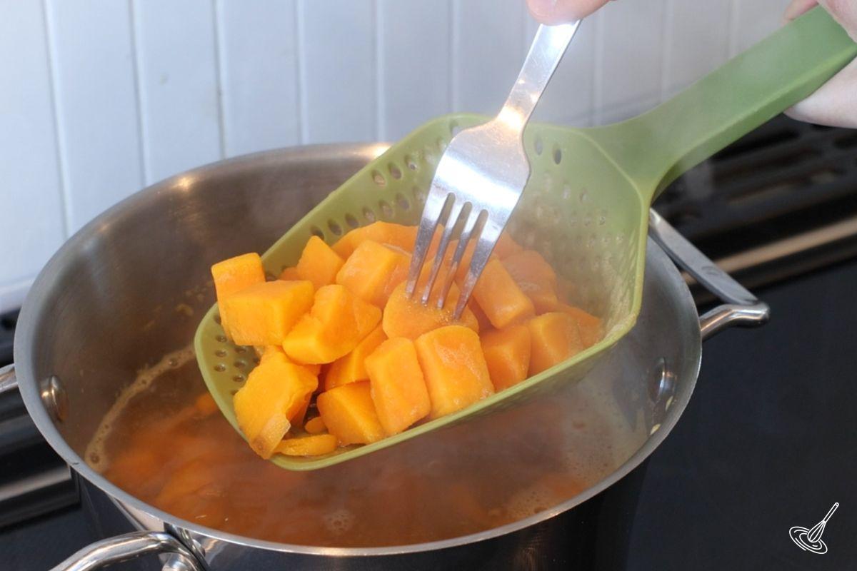 Une personne utilise une fourchette pour vérifier la cuisson des cubes de patate douce.