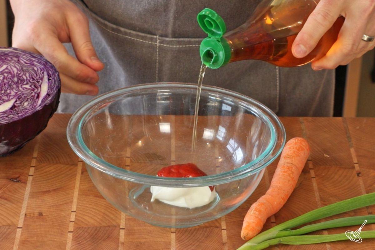 Someone adding apple cider vinegar to a mixing bowl with Greek yogurt and sriracha. 
