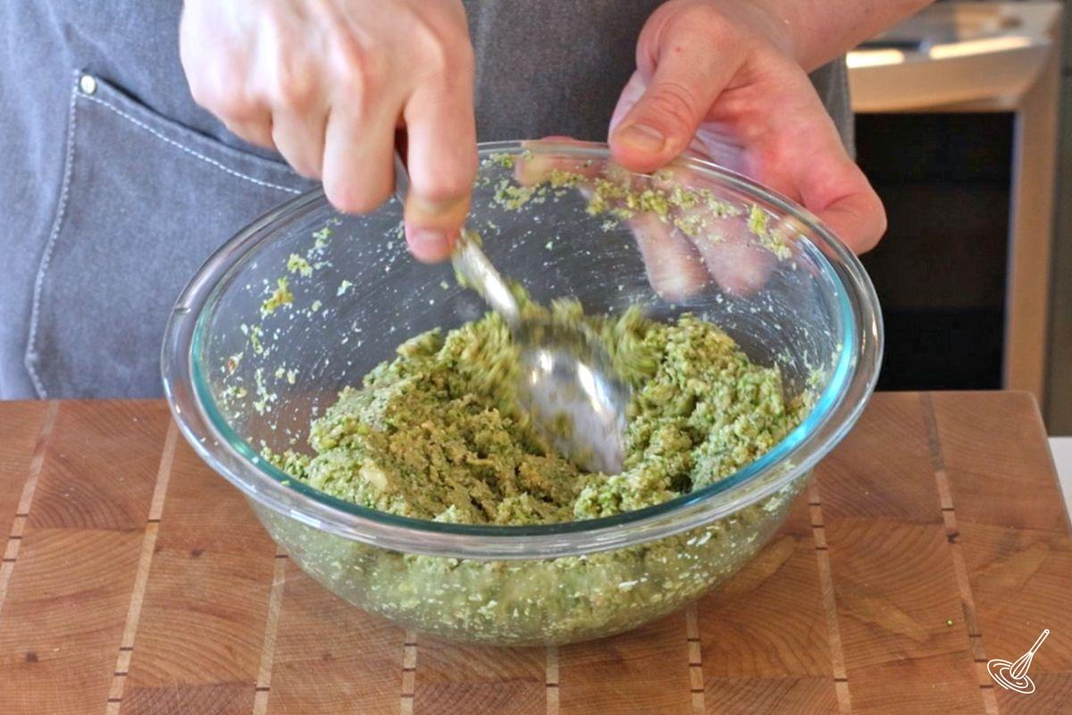 Someone using a spoon to stir a broccoli meatball mixture.