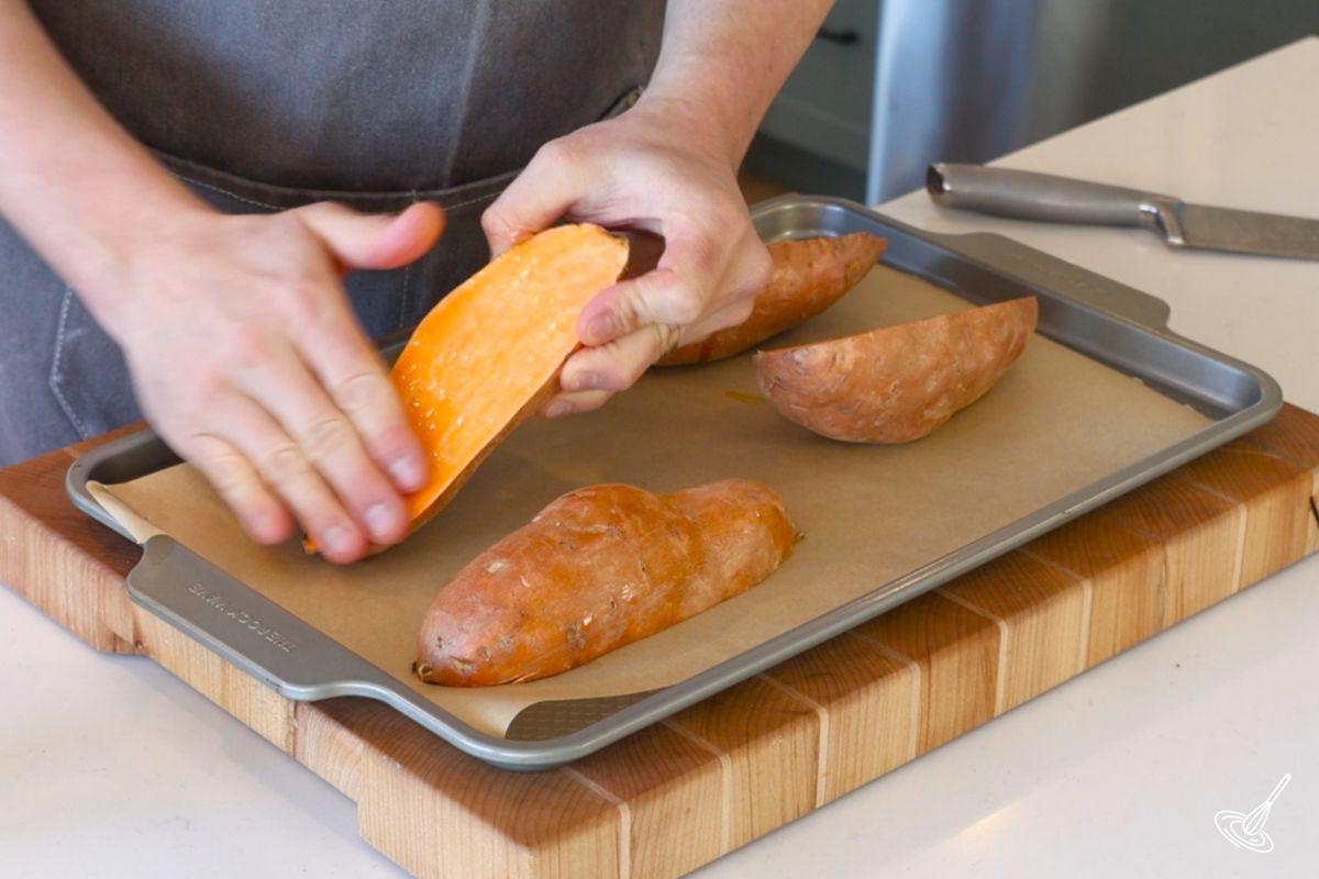 Someone using their hand to spread olive oil on sweet potato halves. 