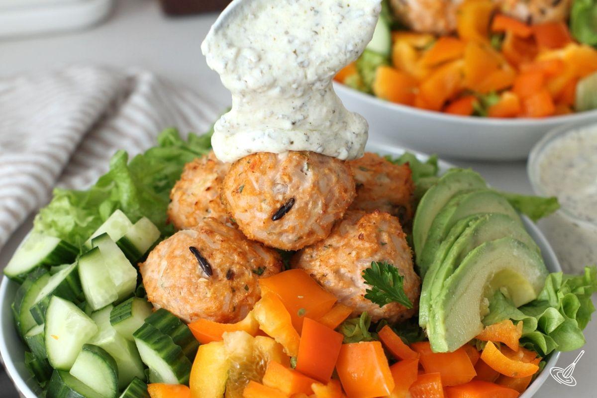 Quelqu'un verse de la vinaigrette sur les boulettes de viande dans une salade. 